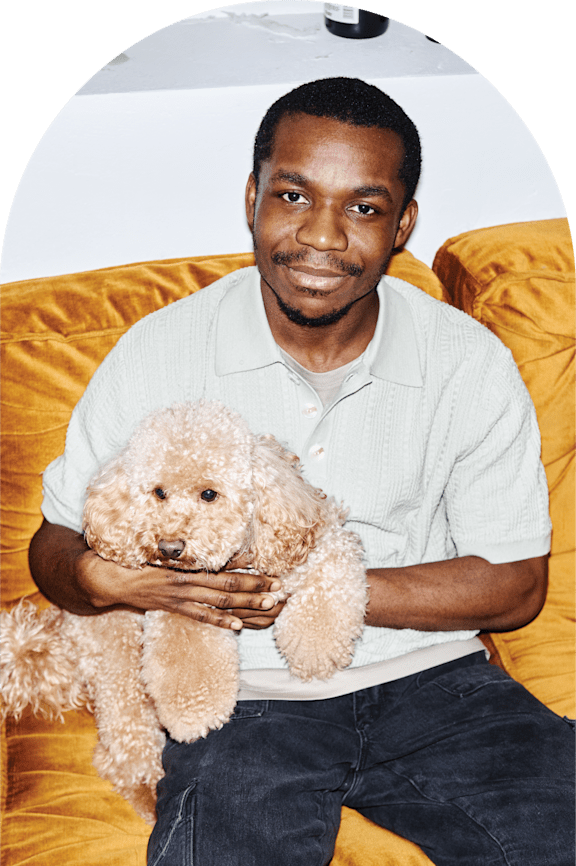 A man is sitting on a yellow couch holding a brown dog.