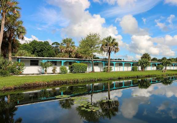 A serene landscape with a building, trees, and a reflective body of water at Golden Shores of Jacksonville in Jacksonville, FL 32211