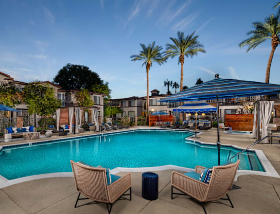 A swimming pool with two chairs and a table in front of a house with a blue sky.