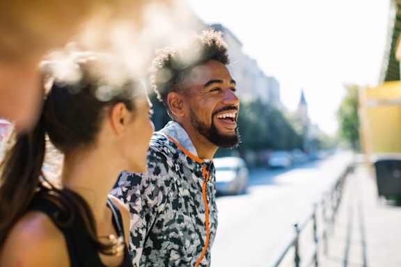 A man with a beard and a patterned shirt is laughing while standing on a street.