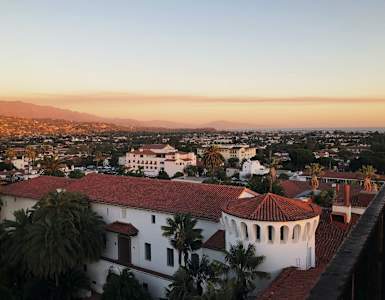 A white building with a red roof is in the foreground of a cityscape.