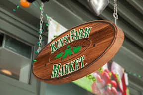 A wooden sign that says "Kin's Farm Market" hanging from a chain.