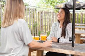 Two women sitting at a table with drinks, one is laughing.