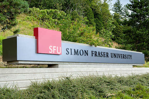 A sign for Simon Fraser University is displayed in front of a forest.