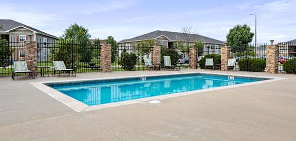 A swimming pool surrounded by a black fence and lawn chairs.