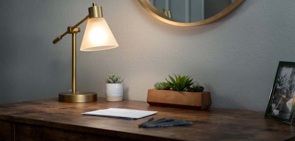 A desk with a lamp, a plant, and a picture frame on it.