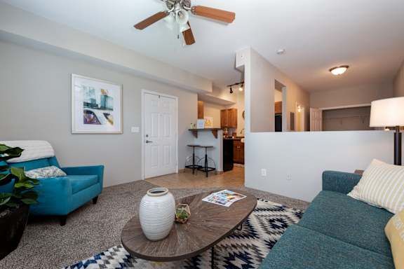 A living room with a blue couch, a white vase, and a ceiling fan.