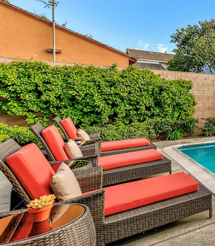 A pool surrounded by a concrete patio and red cushioned chairs.