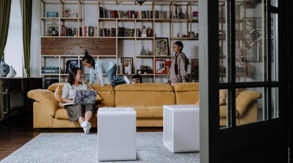A family is sitting on a couch in a living room with bookshelves in the background.