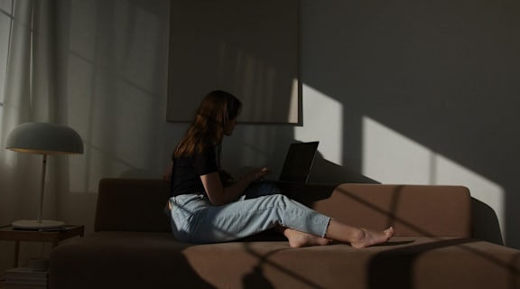 A woman is sitting on a couch with a laptop.