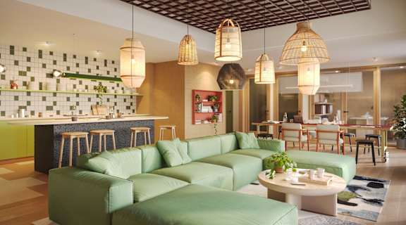 A living room with a green sofa and a kitchen area in the background.
