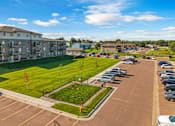 Thumbnail 10 of 10 - A parking lot with cars and a grassy area in front of a building.