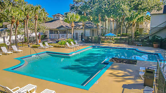 A large swimming pool surrounded by lounge chairs and palm trees.