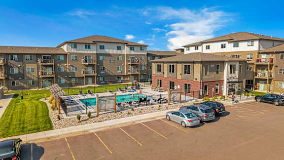 A sunny day at a parking lot with cars and apartment buildings.