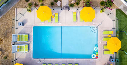 An aerial view of a swimming pool surrounded by yellow umbrellas and lounge chairs.