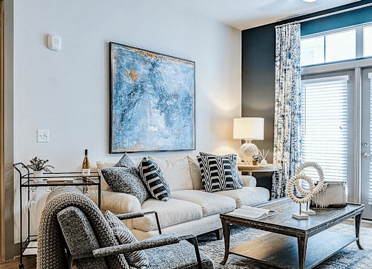 A modern living room with a grey chair, a white sofa, and a large painting on the wall.