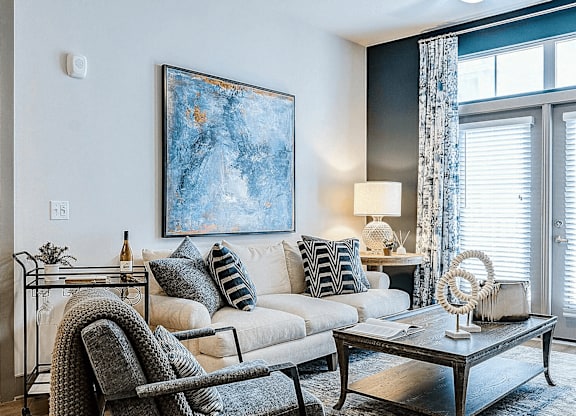 A modern living room with a grey chair, a white sofa, and a large painting on the wall.
