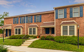 An exterior view of Severgn Apartments two-story buildings with well-maintained lawns, beautiful landscaping, and street lamps lining a sidewalk.