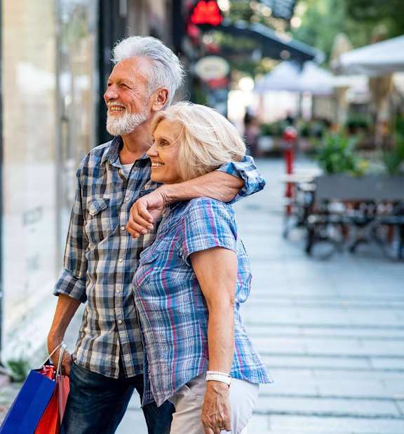 An older couple is walking down the street holding hands and shopping bags.