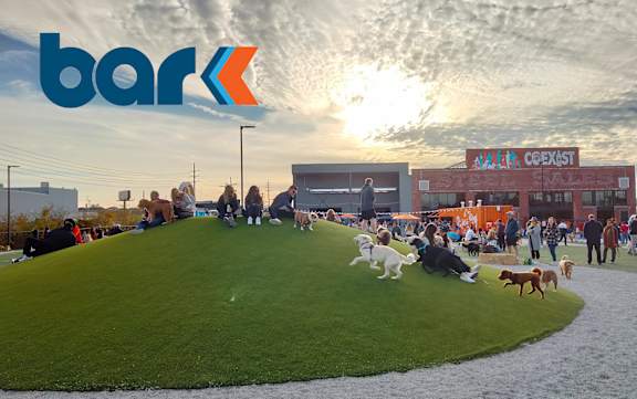 A group of people are sitting on a grassy hill with a building in the background.