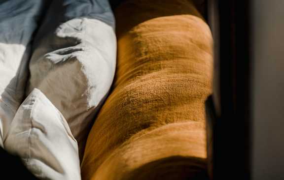 A close up of a bed with a white pillow and a brown blanket.