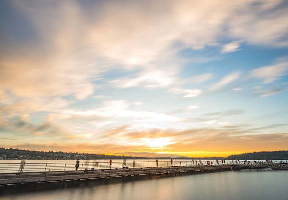 a person walking on a bridge over the water at sunset