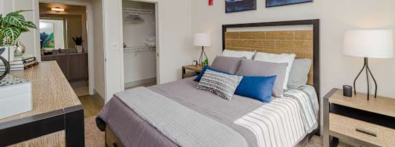 A bedroom with a bed, nightstand, and a plant.