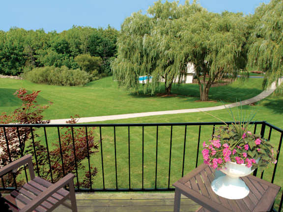 A balcony with a table and chairs overlooking a green lawn.