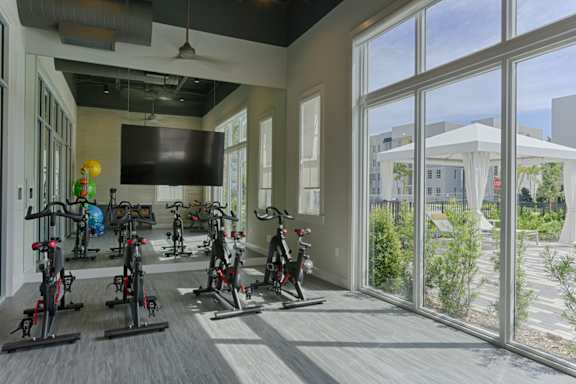 A room with a row of stationary bikes and a television mounted on the wall.