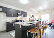Thumbnail 2 of 7 - A kitchen with a white counter top and wooden chairs.