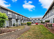 Thumbnail 1 of 8 - A row of grey apartment buildings with a walkway in the middle.