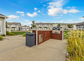 Thumbnail 6 of 10 - A residential area with a brown house and a grey trash bin.