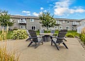 Thumbnail 5 of 10 - A concrete patio with a table and chairs in front of a grey apartment building.