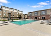 Thumbnail 3 of 10 - A swimming pool is surrounded by sun loungers in front of apartment buildings.