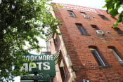 Thumbnail 28 of 28 - Upshot of large brick building in Pasadena CA. Two large signs saying "Brookmore apts" and "Brookmore Apartments" on building with green trees in front.