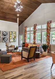 A living room with a wooden floor and a large window with orange curtains.