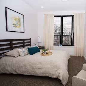 A bedroom with a bed, chair, and window.