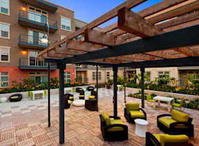A patio with a wooden pergola and black and yellow chairs.