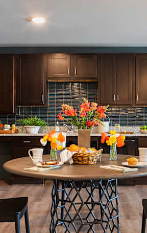 A kitchen with a table set for two with flowers in the middle.