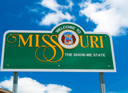A green sign that says "Welcome to Missouri, the Show-Me State" with a picture of the state seal in the center.
