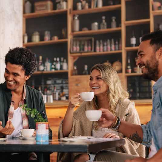 Four people are having a conversation over coffee in a cozy café setting.