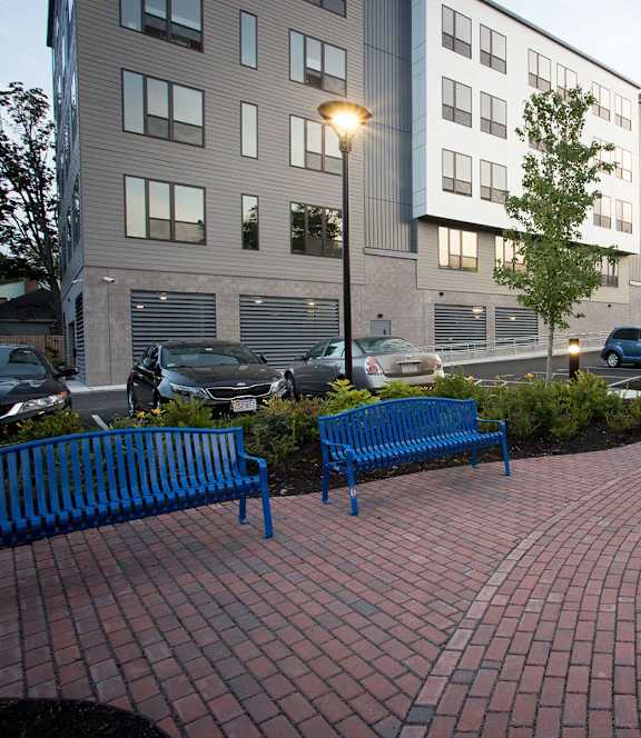 A brick walkway leads to a building with a blue bench on the left.
