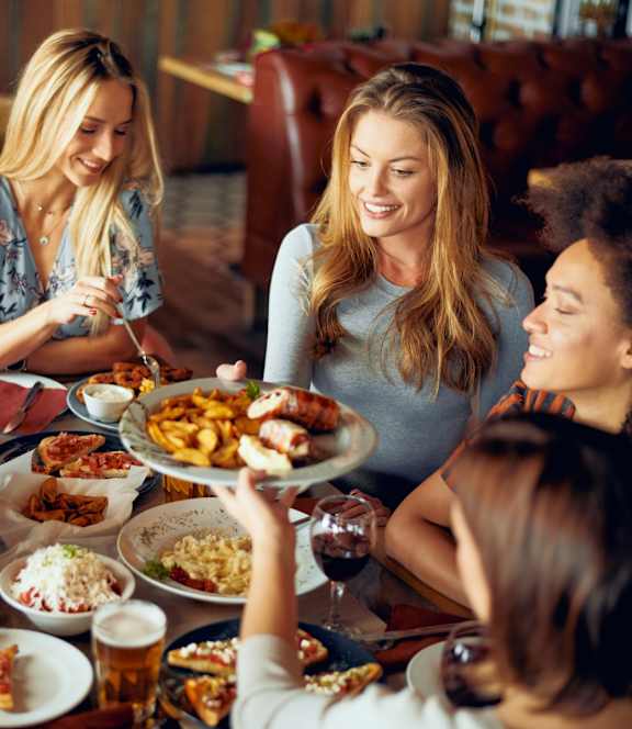 A group of people are gathered around a table full of food and drinks.