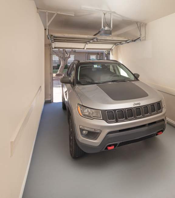 A grey Jeep is parked in a long, narrow garage.
