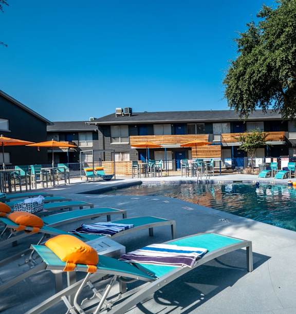 A pool area with sun loungers and a building in the background.