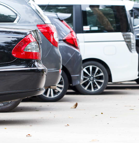 A white car is parked between a grey car and a black car.