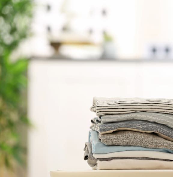 A stack of towels sits on a table next to a blue pitcher.