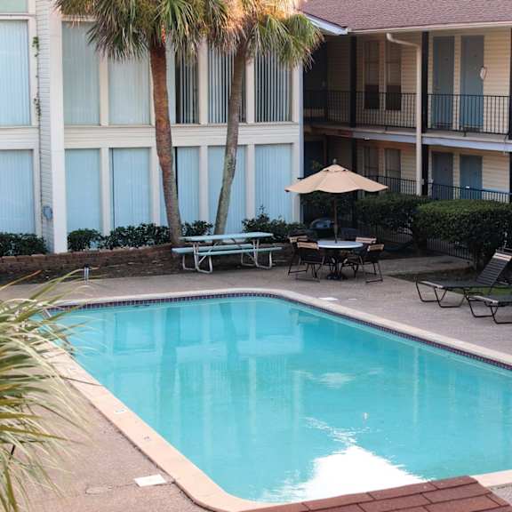 A pool surrounded by chairs and a building with blue doors.
