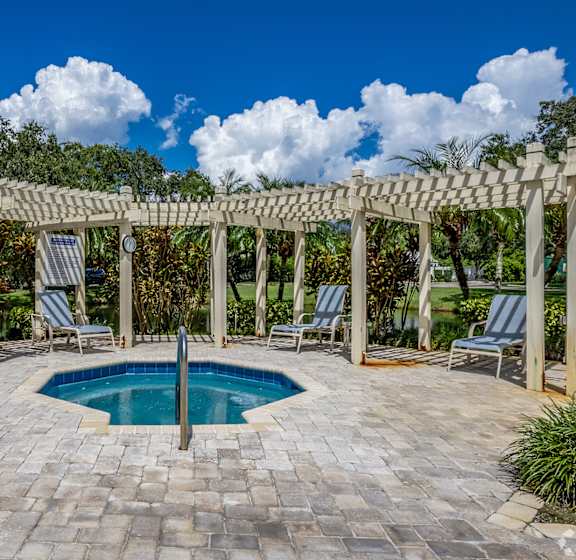 A pool surrounded by a pergola and chairs.