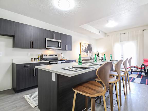 A kitchen with a white counter top and wooden chairs.